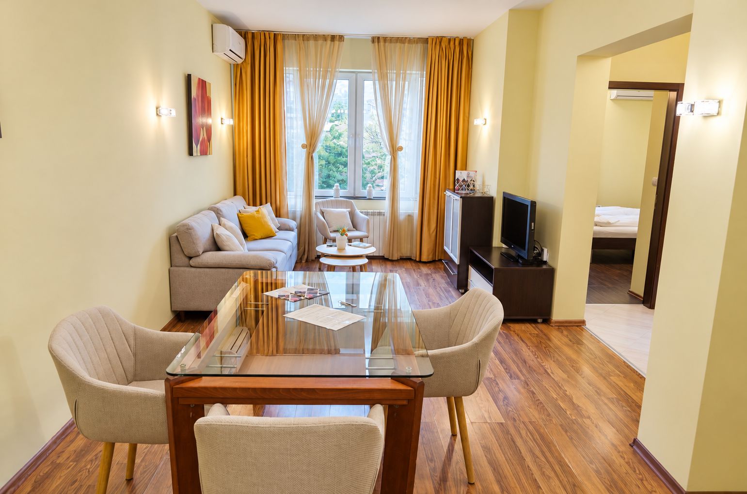 A modern living room with a glass coffee table, two armchairs, a sofa, and a television.