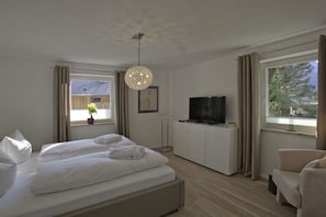 A bedroom with a bed, a television, a dresser, and a window with curtains. - Alpine Jewel Garmisch (Garmisch-Partenkirchen)