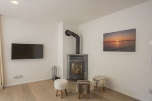 A modern living room with a fireplace, a flat-screen TV, and a sunset painting. - Alpine Jewel Garmisch (Garmisch-Partenkirchen)