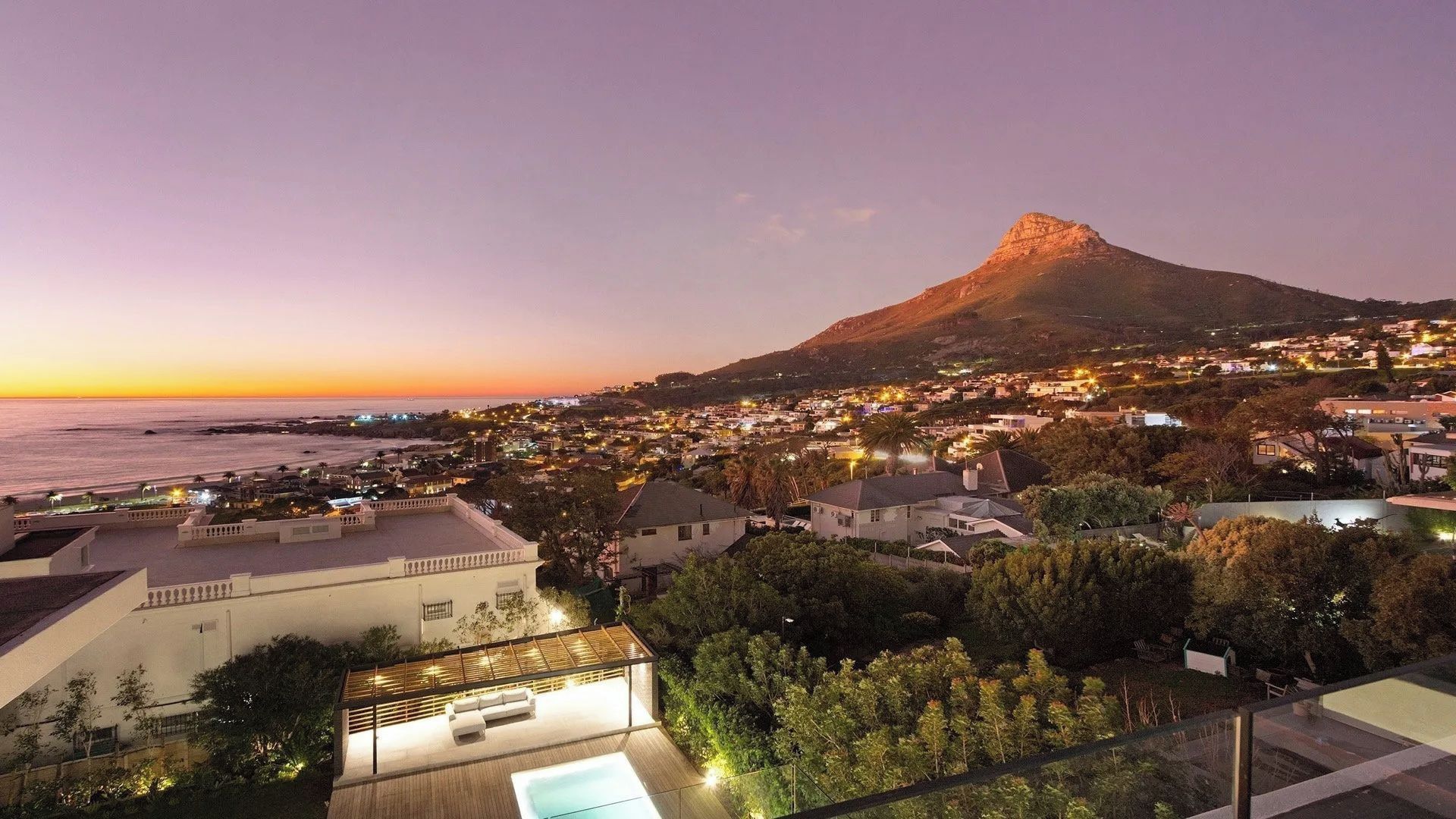 Une ville côtière au crépuscule, avec une montagne imposante en arrière-plan.