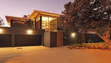 Une maison moderne à deux étages, dotée d’un garage, de grandes fenêtres et d’un arbre dans le jardin.