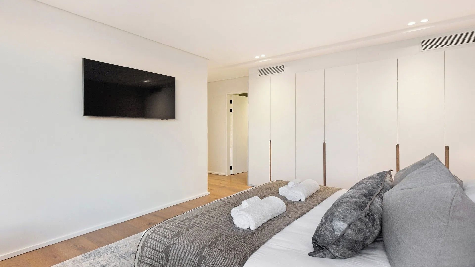 Une chambre moderne avec un lit, des oreillers, un téléviseur à écran plat et une armoire.
