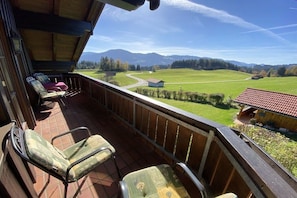 Ein Balkon mit Stühlen, einem Holgitter und Blick auf ein grünes Feld und Berge.