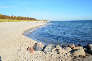 Ein sandiger Strand mit felsiger Küstenlinie und ruhigem Wasser.