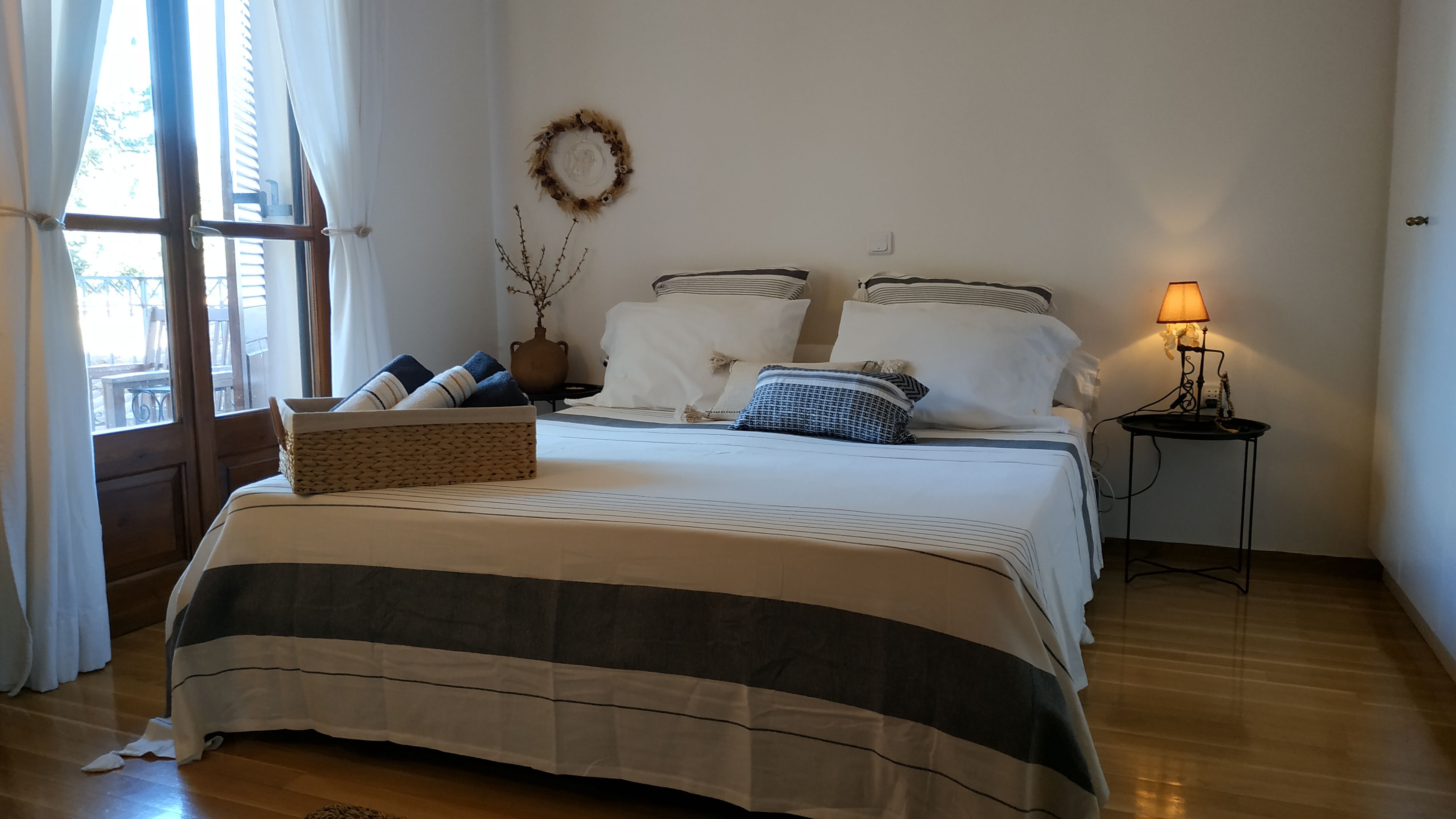 A neatly made bed with a striped bedspread, a bedside lamp, and a vase with branches on the nightstand.
