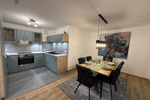A modern kitchen with a dining area, featuring a wooden table and chairs, a painting on the wall, and a ceiling light fixture. - Willi's holiday apartment (Kressbronn)