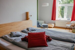 A bedroom with a bed, pillows, a bedside table, a lamp, a window with curtains, and a view of greenery outside. - Holiday apartment in Loit with swimming pool (Loit)