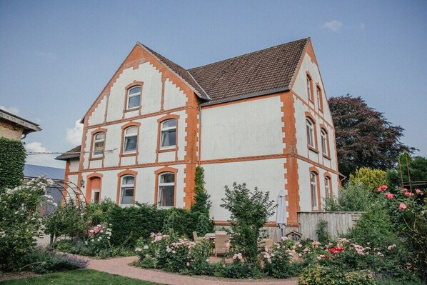 A two-story house with a garden in front, featuring a pathway and various plants. - Holiday apartment in Loit with swimming pool (Loit)