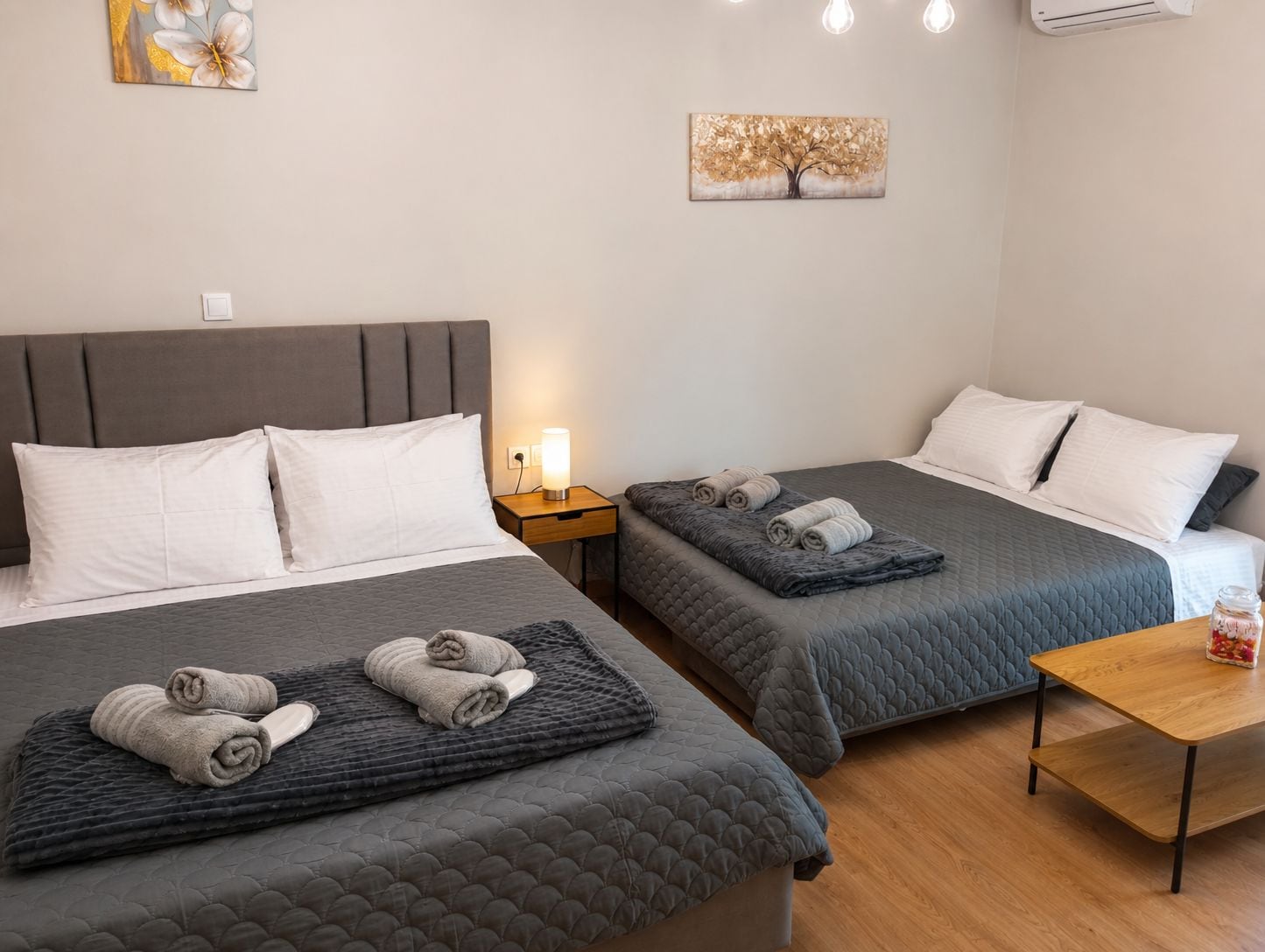 A hotel room with two beds, a nightstand, a table, and artwork on the walls.