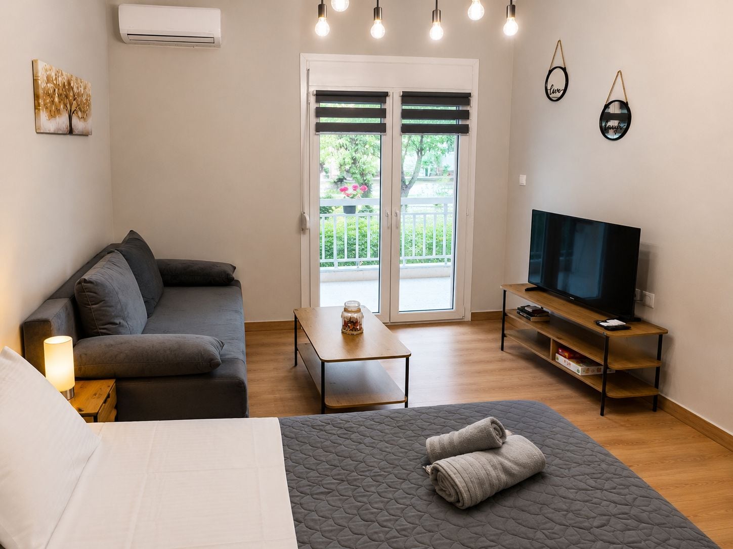 A modern bedroom with a bed, a sofa, a TV, and a balcony with a view.