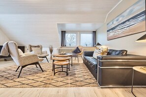 Una sala de estar moderna con un sofá, sillones, una mesa de centro y un cuadro grande en la pared.