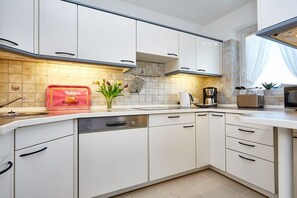 Una cocina moderna con armarios blancos, lavavajillas y una encimera con tostadora y cafetera.
