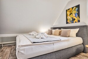 A bedroom with a bed, pillows, a blanket, a radiator, and a painting on the wall. - Holiday apartment in Sylt with 2 bedrooms (Westerland)