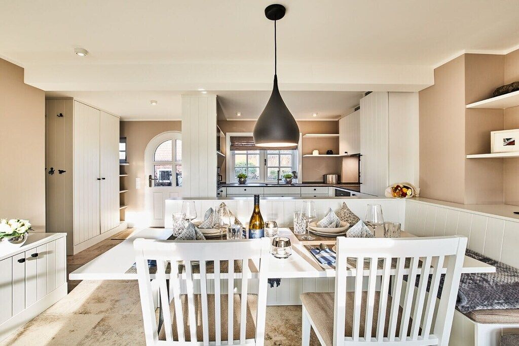 Una cocina moderna con armarios blancos, una isla central con asientos y una lámpara colgante.