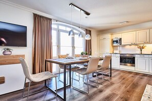 A modern kitchen with a dining area, wooden flooring, and a flat-screen TV mounted on the wall. - Holiday apartment in Sylt with 3 bedrooms (Westerland)