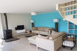 Un salon moderne avec un canapé beige, un téléviseur, une cheminée et un mur d’accent bleu.