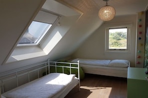 Ein Schlafraum im Schlafsalstil mit zwei Betten, einem Dachfenster und Blick auf Grünflächen.