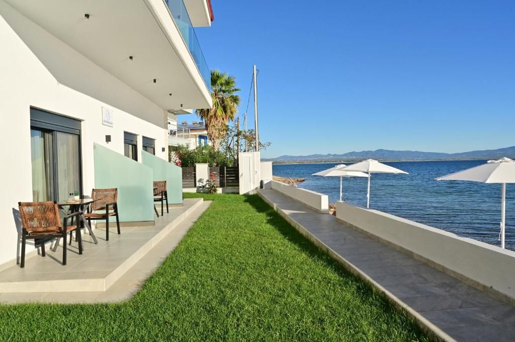 Un balcón de hotel con vistas al mar, mobiliario exterior y un césped cuidado.