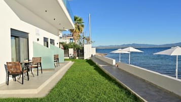 Un balcón de hotel con vistas al mar, mobiliario exterior y un césped cuidado.