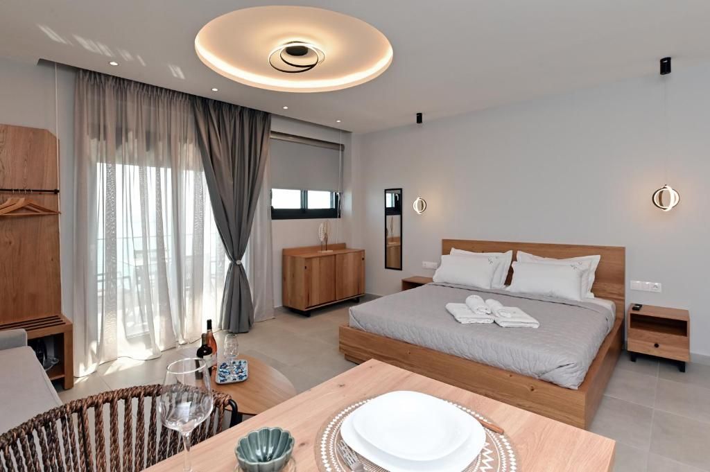 Un dormitorio moderno con una cama grande, mesitas de noche, un armario de madera, una zona de comedor con mesa y sillas, y un amplio ventanal con cortinas.
