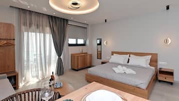 Un dormitorio moderno con una cama grande, mesitas de noche, un armario de madera, una zona de comedor con mesa y sillas, y un amplio ventanal con cortinas.