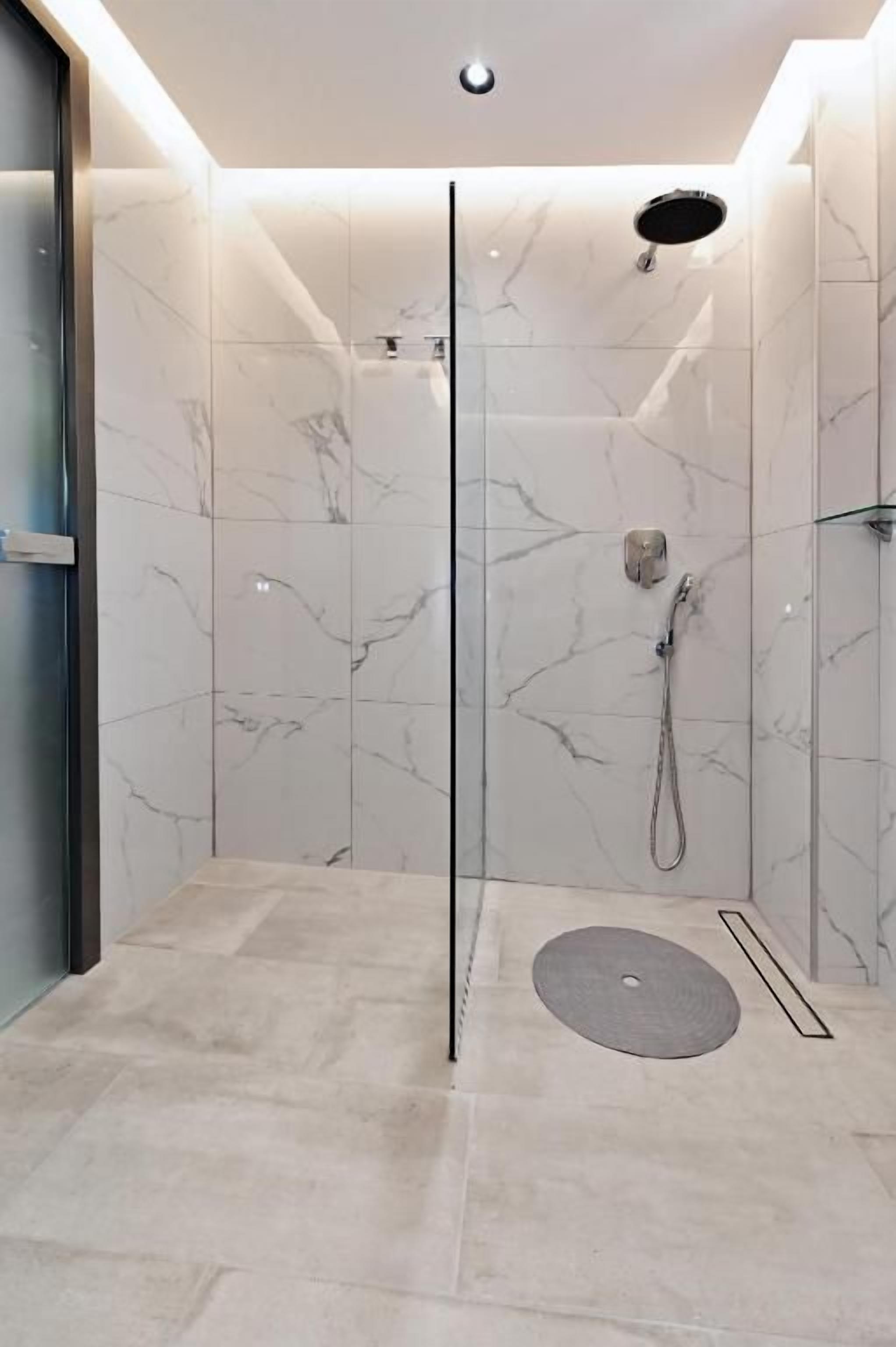 A modern shower with a glass door, marble walls, and a floor drain.