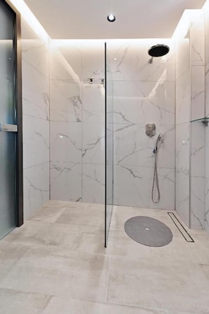 A modern shower with a glass door, marble walls, and a floor drain. - Vista Paraiso Inn (Nea Potidea)