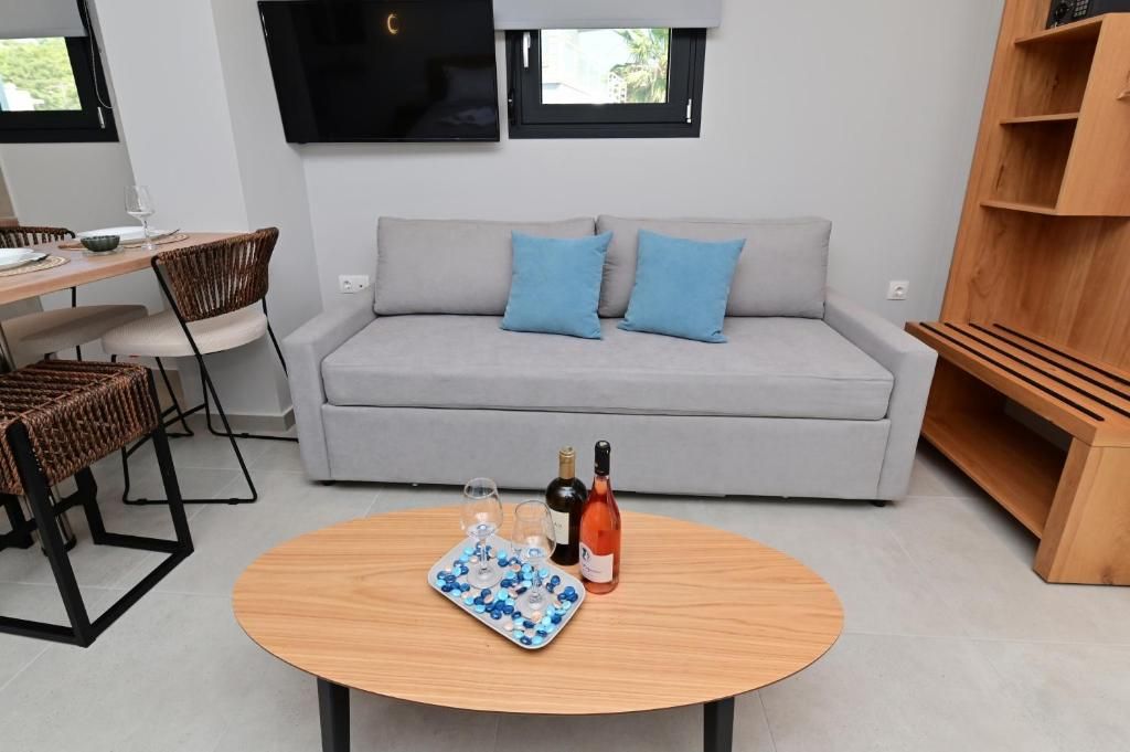 A modern living room with a grey sofa, two blue cushions, a wooden coffee table with wine glasses and a bottle, and a TV mounted above a window.