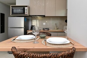 A dining area with a wooden table set for two, two chairs, a microwave, and a refrigerator.