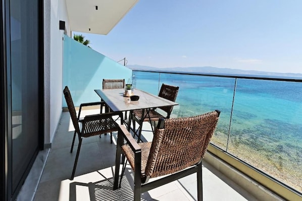 A balcony with a table and chairs overlooking a clear blue sea.
