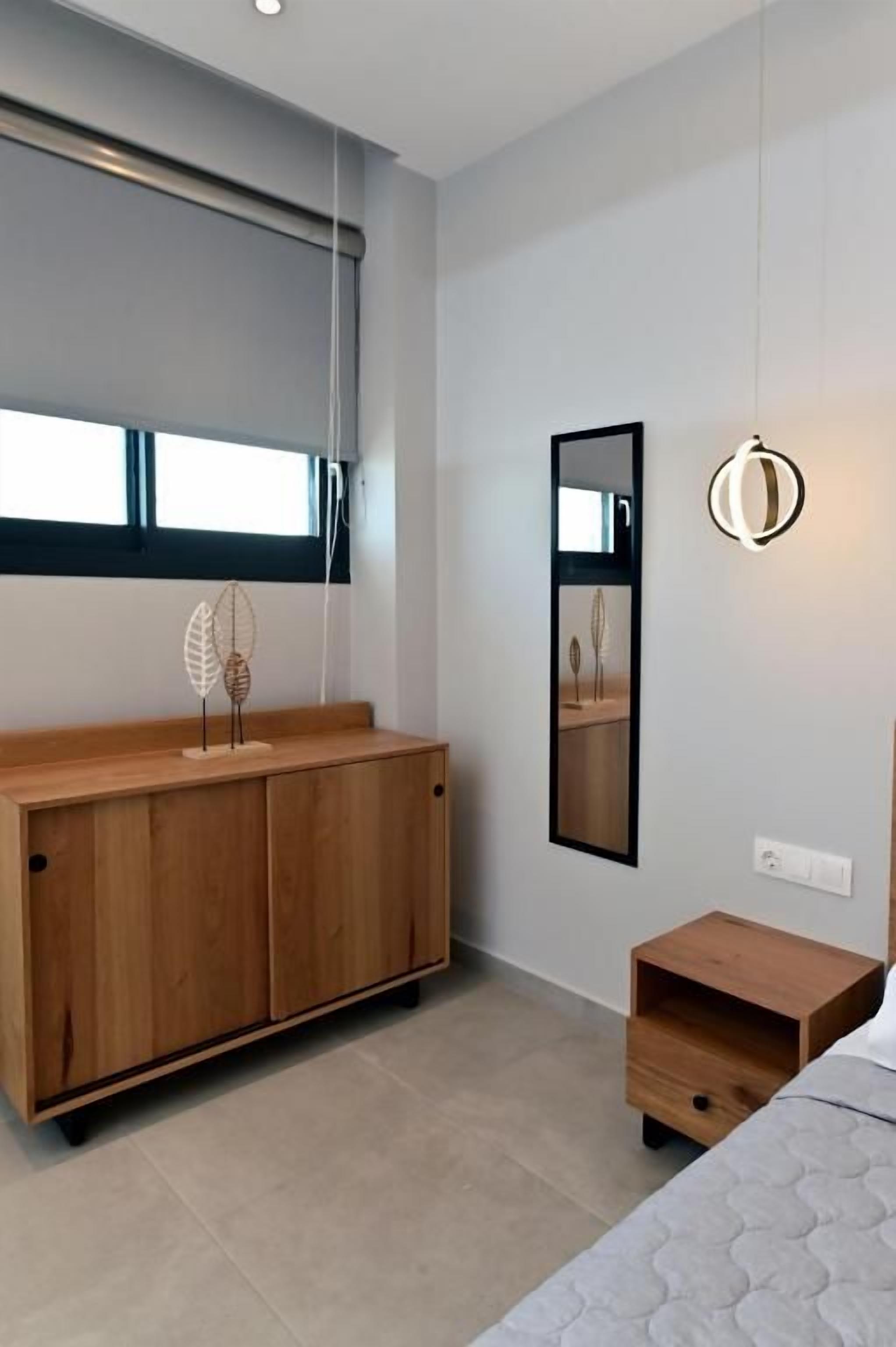 Un dormitorio moderno con un aparador de madera, una mesita de noche, un espejo y una lámpara colgante.