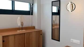 Un dormitorio moderno con un aparador de madera, una mesita de noche, un espejo y una lámpara colgante.