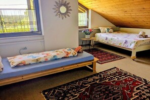 Ein Zimmer mit zwei Betten, einem kleinen Tisch und einem Fenster mit Vorhängen.
