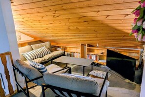 A cozy attic room with a sofa, a small table, a TV, and bookshelves. - Holiday home with 2 bedrooms (Herdwangen-Schönach)