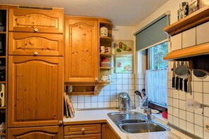 Eine Küche mit Holzschränken, einer Edelstahl-Spüle und einem Fenster mit Blick ins Grüne.