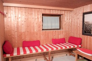 A wooden cabin with a bench and two red cushions, a small window with a curtain, and a framed picture on the wall. - Holiday home with 2 bedrooms (Herdwangen-Schönach)