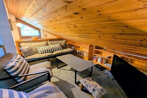 Ein gemütliches Loft-Zimmer mit Holzboden, einer Couch, einem Couchtisch, einem Bücherregal und einem Fernseher.