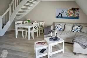 Ein modernes Wohnzimmer mit Treppe, Essbereich und einer Couch mit gemusterten Kissen.