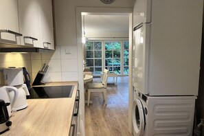 A modern kitchen with a built-in oven, a washing machine, and a dining area with a table and chairs. - Holiday apartment with 1 bedroom (Sankt Peter-Ording)