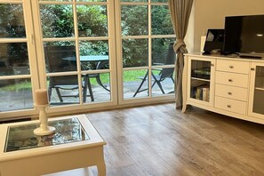 A room with a large window, a television on a cabinet, and a table with a candle. - Holiday apartment with 1 bedroom (Sankt Peter-Ording)