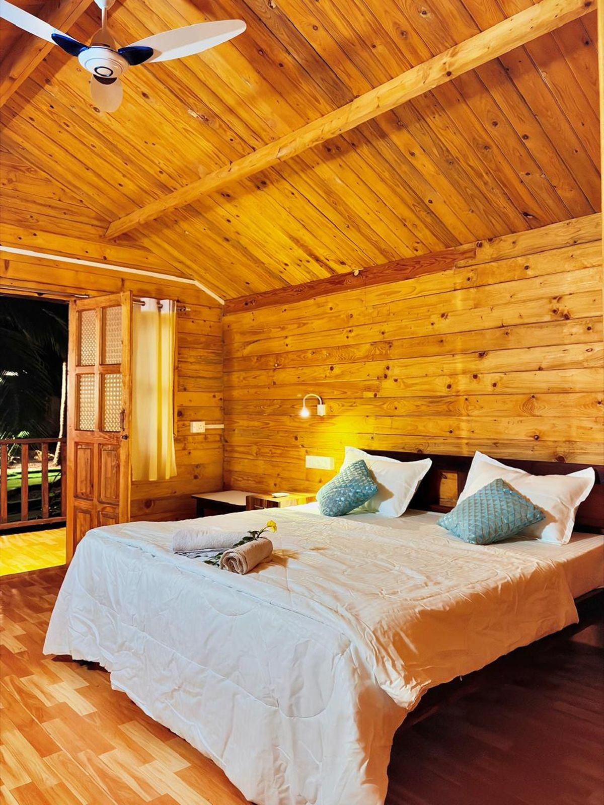 A wooden cabin bedroom with a bed, pillows, a ceiling fan, and a door leading outside.