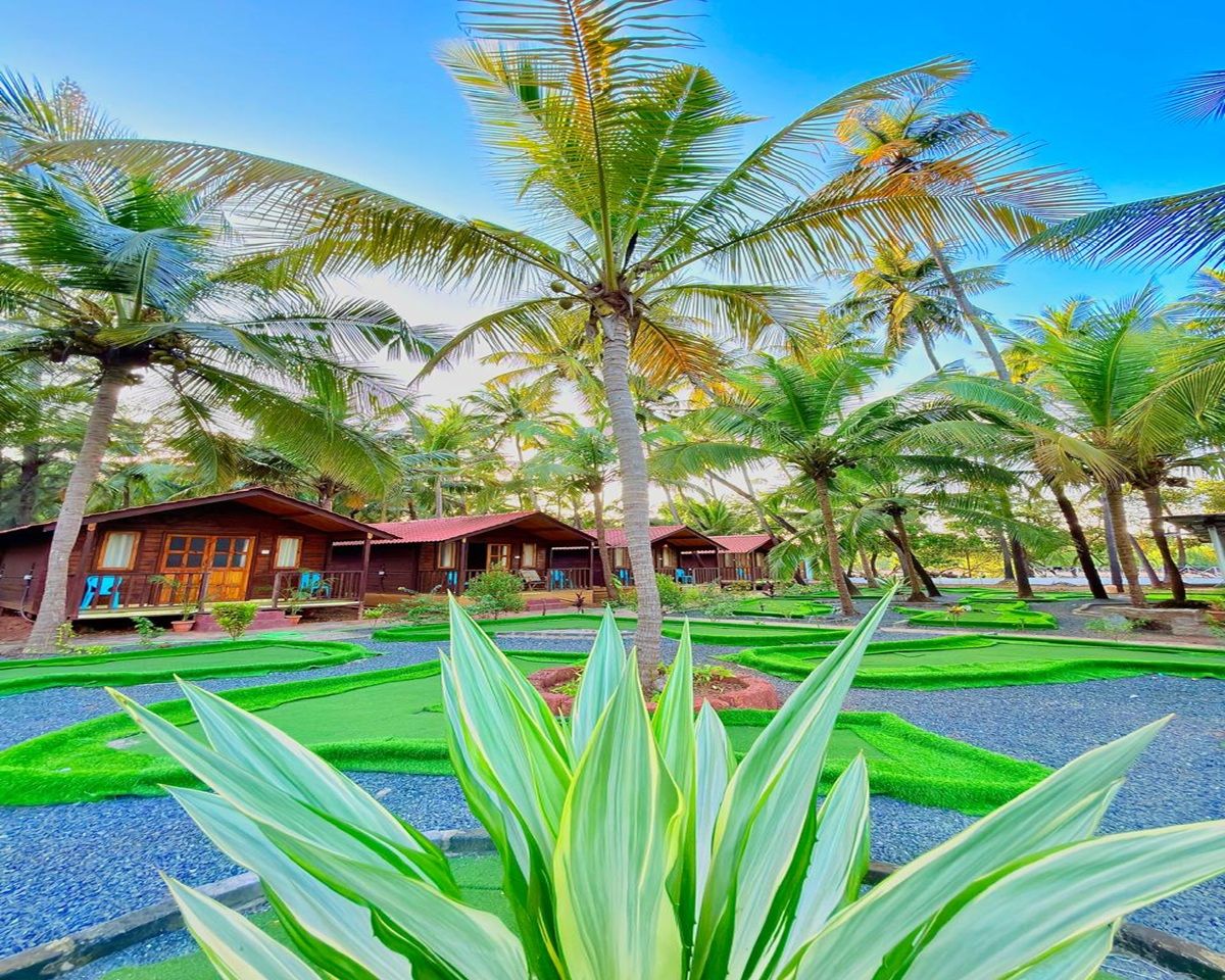 A resort with multiple wooden cabins, surrounded by palm trees and well-manicured lawns.