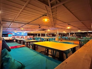 Un comedor interior con mesas y sillas, una barra con un menú, y un techo con vigas a la vista y luces colgantes.