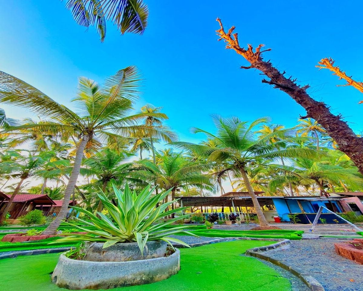 Un hotel tropical amb palmeres, una zona de piscina i un edifici amb teulada vermella.