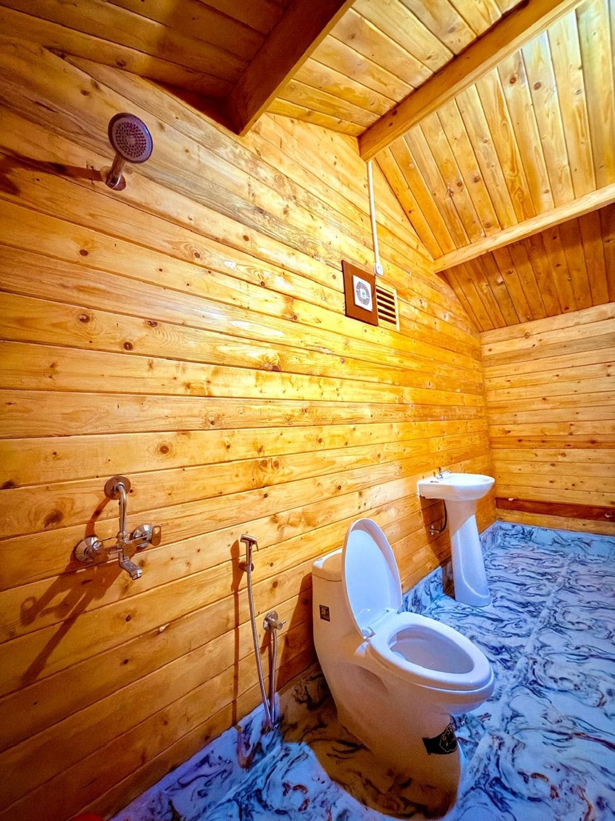 A wooden cabin bathroom with two toilets, a sink, and a shower.