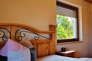 A bedroom with a wooden headboard, a window with blinds, a bedside table with a lamp, and a bed with pillows. - Holiday home in Kail with swimming pool (Kail)