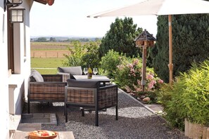 An outdoor seating area with wicker furniture, a table with a bottle and glasses, and a birdhouse. - Holiday home in Kail with swimming pool (Kail)