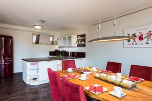 A dining area with a wooden table set for four, red upholstered chairs, a kitchen in the background, and a wall-mounted light fixture. - To the cheerful day laborer (Quedlinburg)