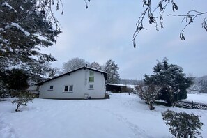 Ein eingeschossiges Haus mit geneigtem Dach, einem sichtbaren Schornstein und einer kleinen Veranda.