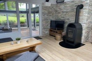 Een moderne woonkamer met een stenen muur, een televisie, een open haard en een groot raam met uitzicht op een tuin.